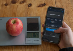 Person wiegt einen Apfel und trägt die Kalorien in ein App ein