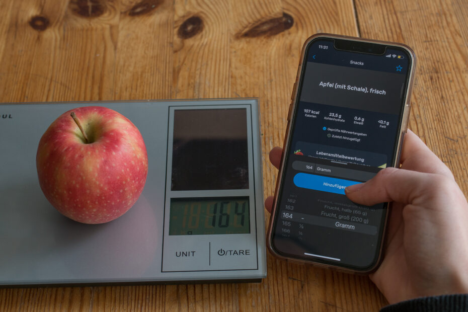 Person wiegt einen Apfel und trägt die Kalorien in ein App ein